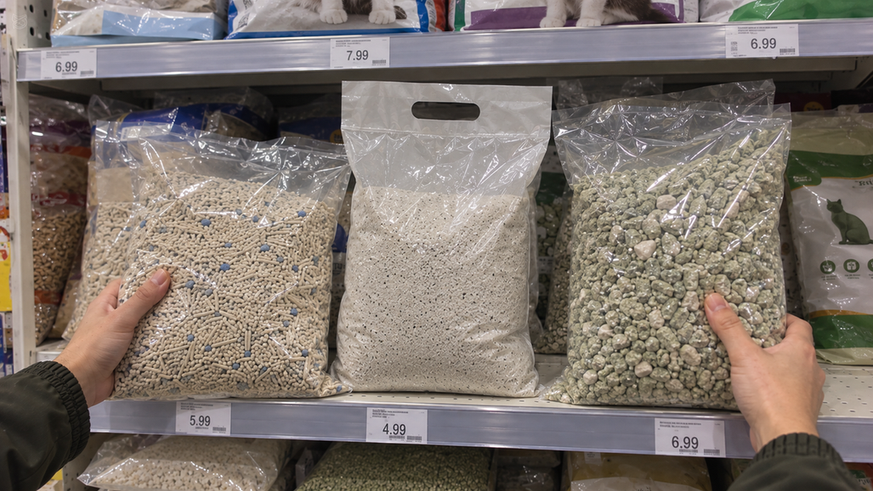 Hands comparing three unbranded cat litter bags in a pet-store aisle