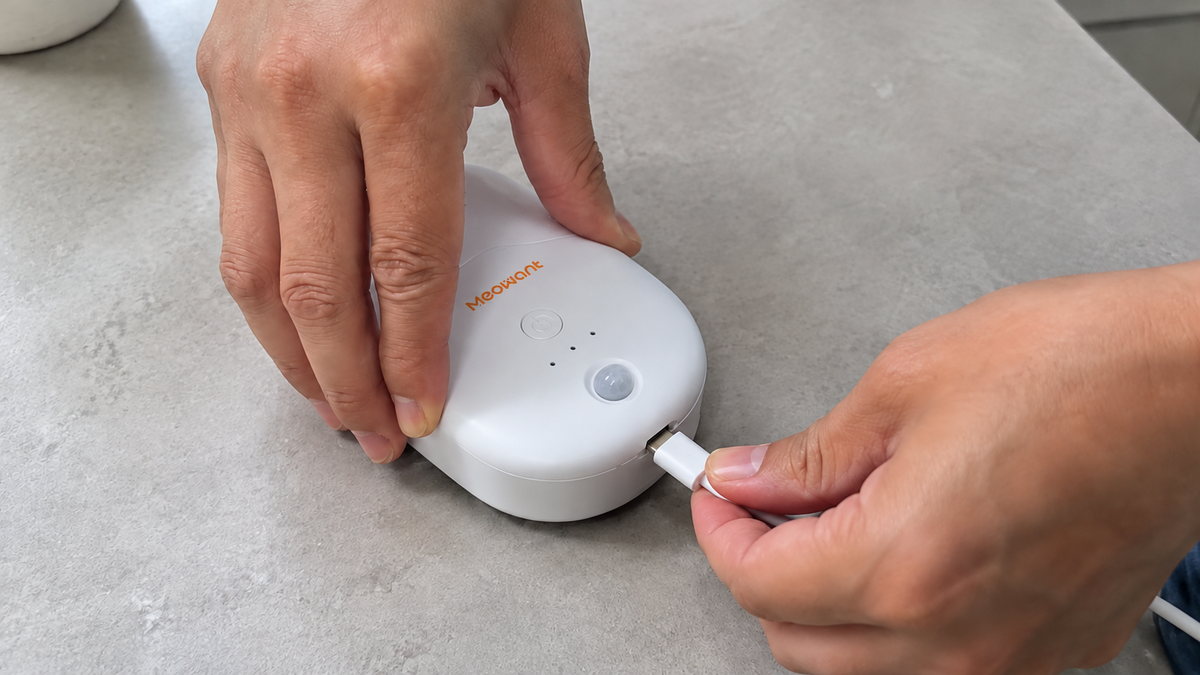 Hands connecting a charging cable to a litter deodorizer on a light gray countertop